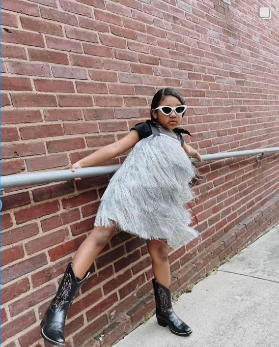 The Tinsel dress, a sparkling party gown with hand-cut tinsel arranged in rows for the perfect shimmy and shine. Features a nude illusion neckline, faux shoulder tie bows, and a silky soft lining for comfort. Back zipper closure and handcrafted in Brooklyn. Perfect for festive celebrations, weddings, and special occasions.