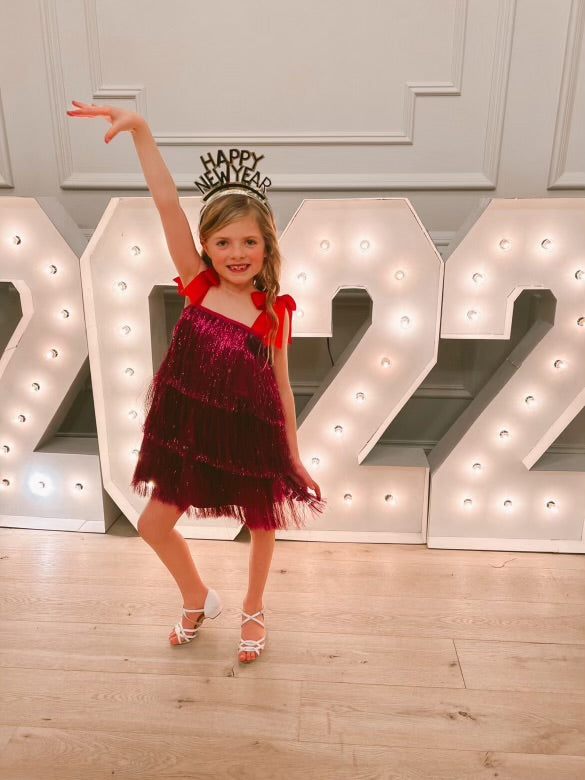 The Tinsel dress, a sparkling party gown with hand-cut tinsel arranged in rows for the perfect shimmy and shine. Features a nude illusion neckline, faux shoulder tie bows, and a silky soft lining for comfort. Back zipper closure and handcrafted in Brooklyn. Perfect for festive celebrations, weddings, and special occasions.