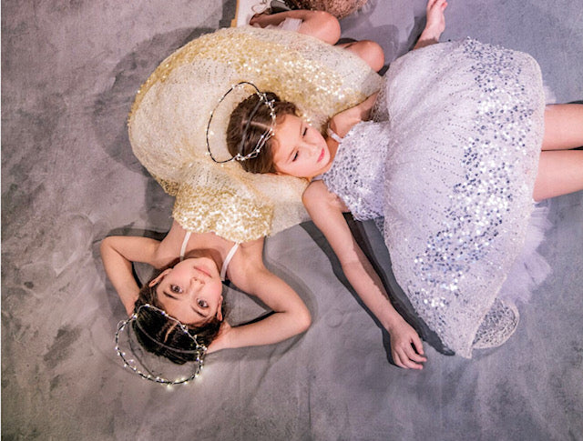 The Constellation flower girl dress, a sparkling gown with glittery paillettes and woven metallic threads over a voluminous petticoat. Features adjustable grosgrain ribbon straps, a back zip closure, and a silky soft lining for comfort. Handcrafted in Brooklyn from silk, tulle, and satin, with optional personalized embroidery. Perfect for weddings, parties, and special occasions.