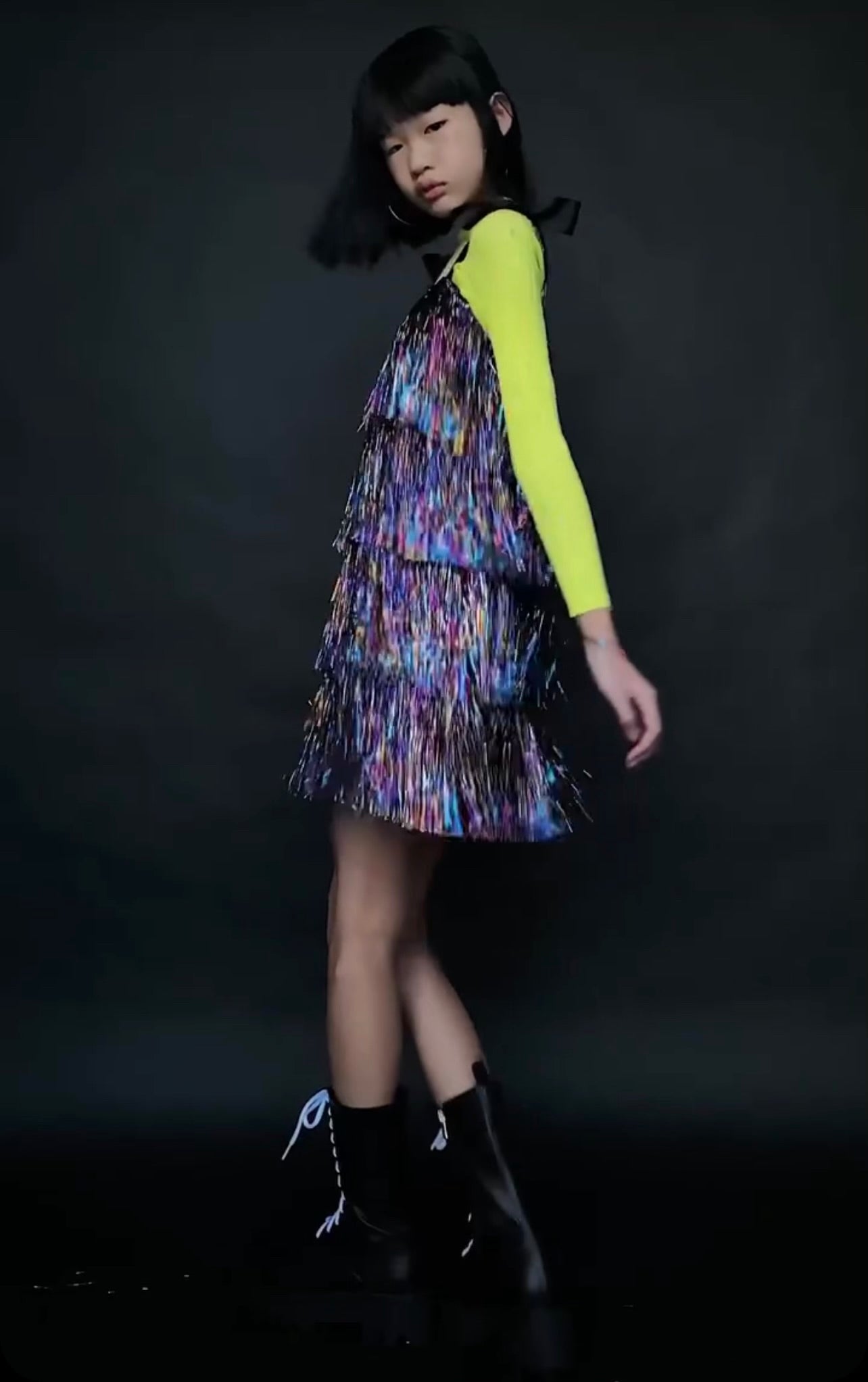 The Tinsel dress, a sparkling party gown with hand-cut tinsel arranged in rows for the perfect shimmy and shine. Features a nude illusion neckline, faux shoulder tie bows, and a silky soft lining for comfort. Back zipper closure and handcrafted in Brooklyn. Perfect for festive celebrations, weddings, and special occasions.