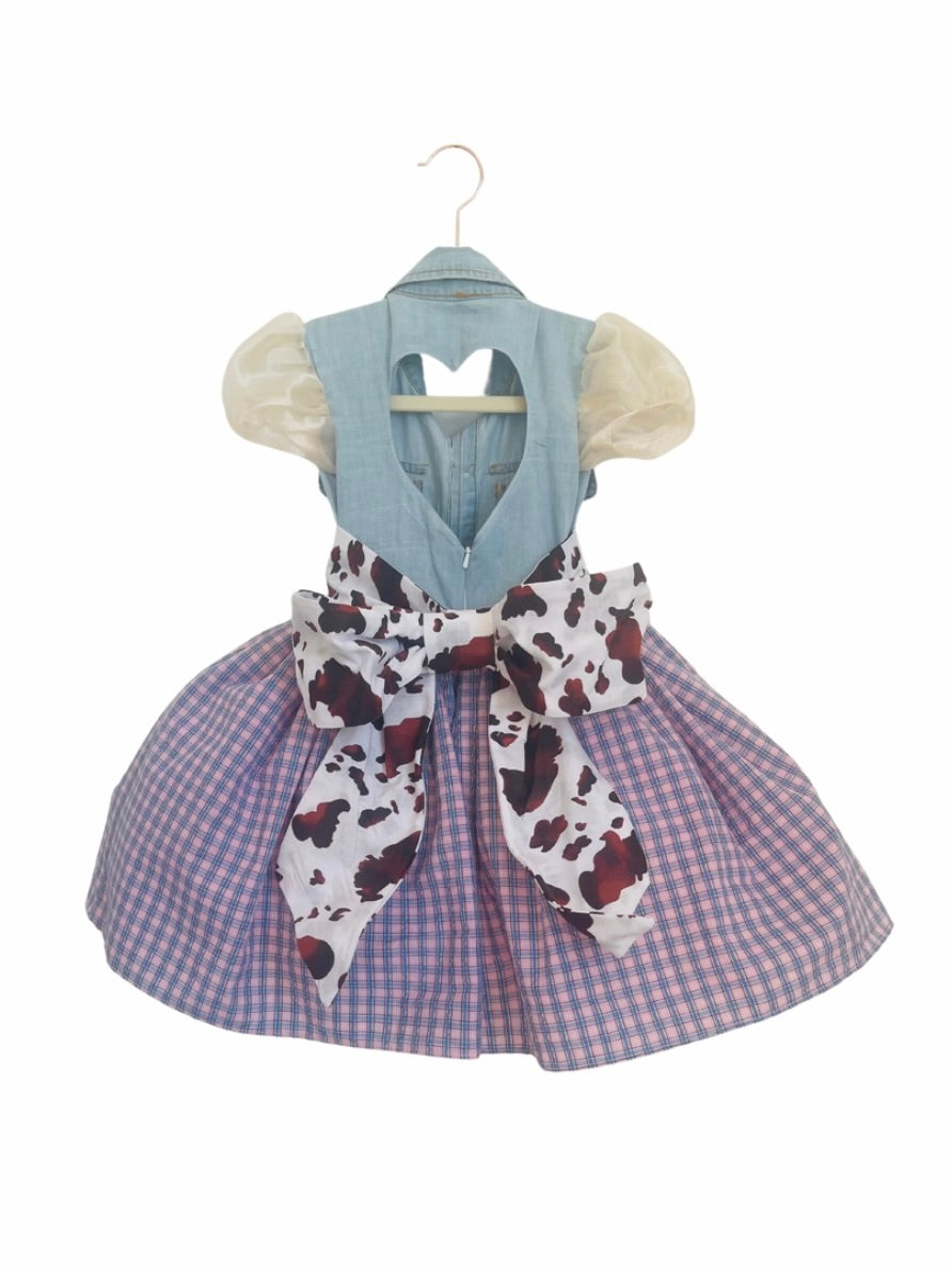 A western-inspired cowgirl dress featuring a denim vest, gingham skirt, cow-print sash, puffed sleeves, and pearl-studded details for a charming look.