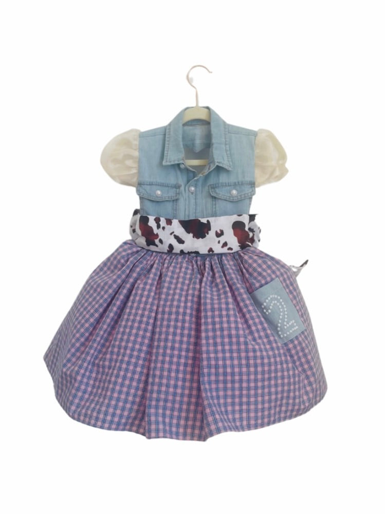 A western-inspired cowgirl dress featuring a denim vest, gingham skirt, cow-print sash, puffed sleeves, and pearl-studded details for a charming look.