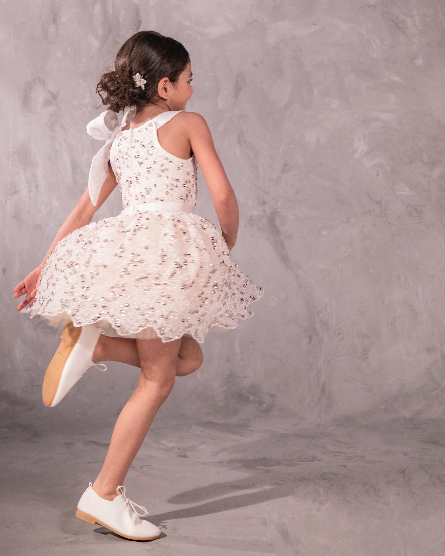 The Katy, a stunning party dress featuring hand-embroidered beading across the bodice and an extra-full skirt for maximum twirl. A velvet ribbon waist and a French-wired silk and brocade shoulder bow add a touch of elegance. Fully lined in silky soft fabric for comfort. Handcrafted in Brooklyn from beaded net, satin, tulle, and silk, with optional personalized embroidery. Perfect for weddings, parties, and special occasions.