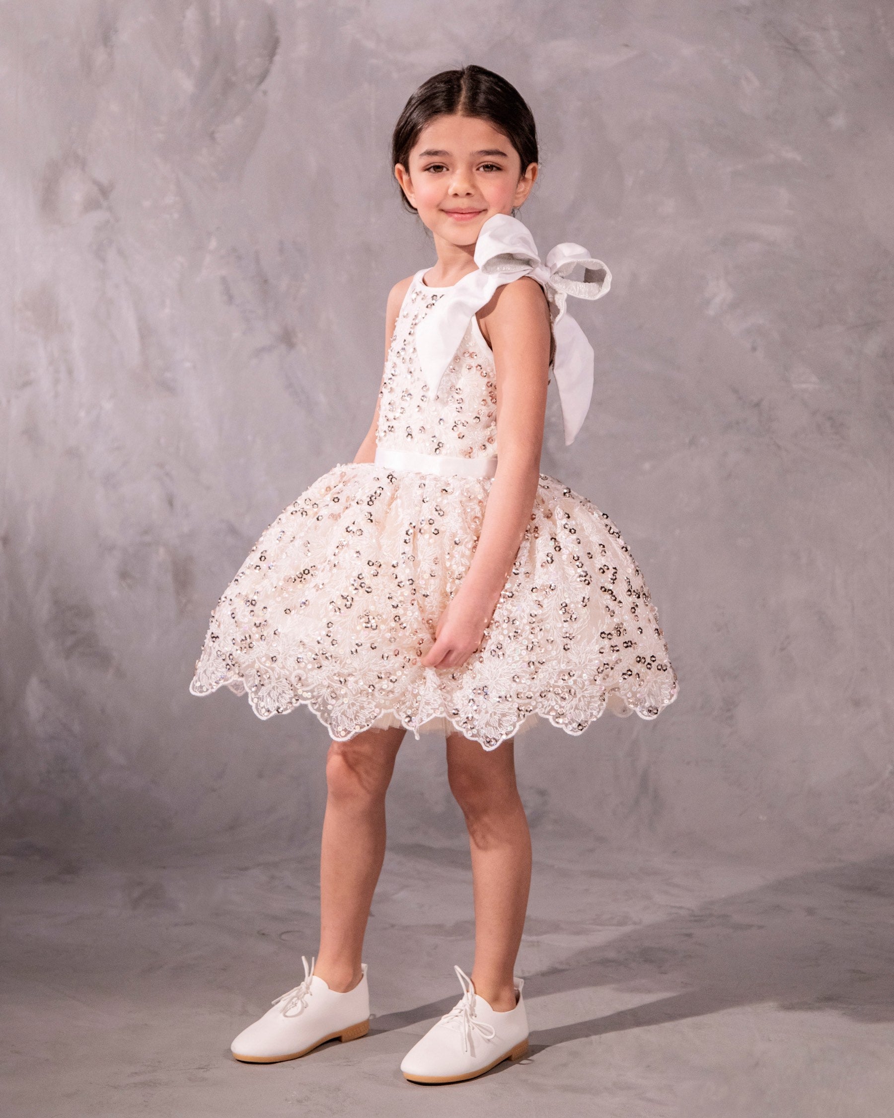 The Katy, a stunning party dress featuring hand-embroidered beading across the bodice and an extra-full skirt for maximum twirl. A velvet ribbon waist and a French-wired silk and brocade shoulder bow add a touch of elegance. Fully lined in silky soft fabric for comfort. Handcrafted in Brooklyn from beaded net, satin, tulle, and silk, with optional personalized embroidery. Perfect for weddings, parties, and special occasions.