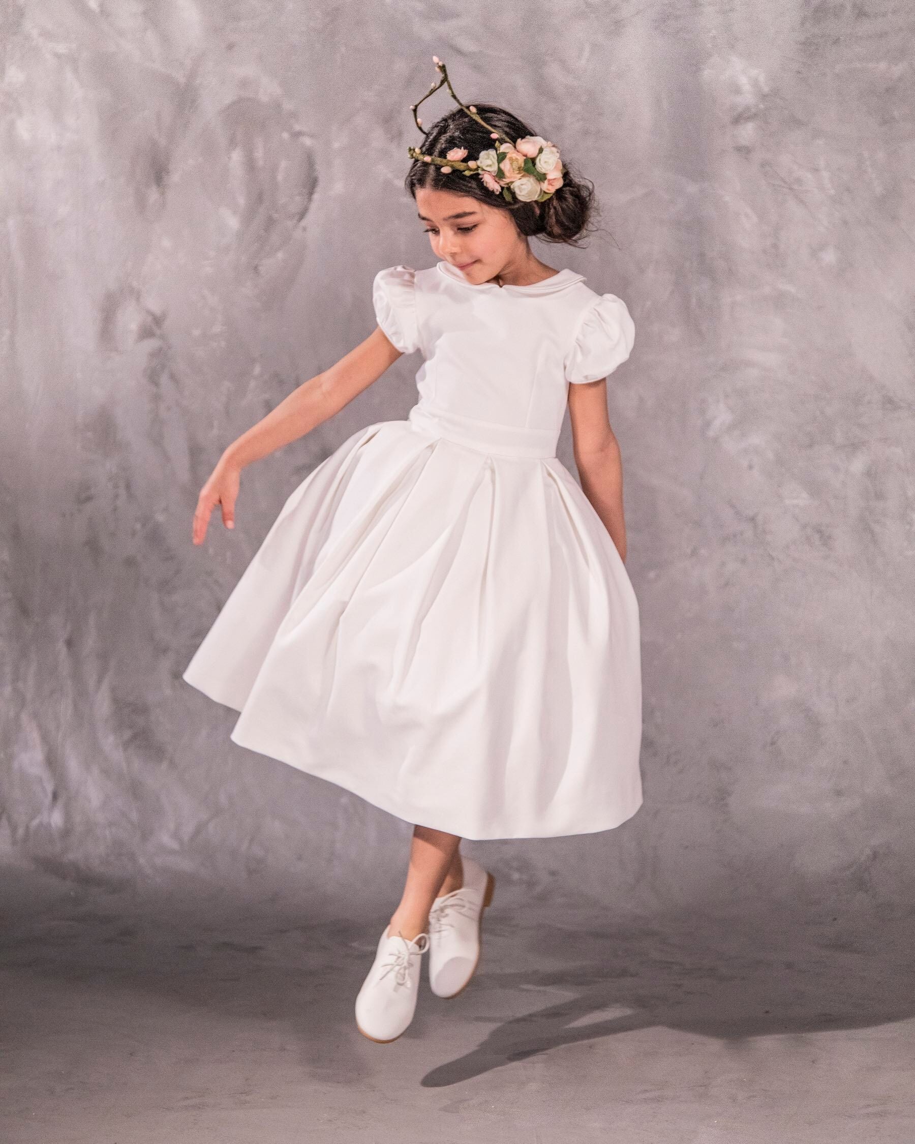 The Rachel – classic flower girl dress with precise seams, puffed sleeves, and a box-pleated skirt. Features a timeless Peter Pan collar, back zip closure, and adjustable petticoat volume. Crafted from satin, silk, and tulle with a silky soft lining, perfect for elegant weddings and special occasions.
