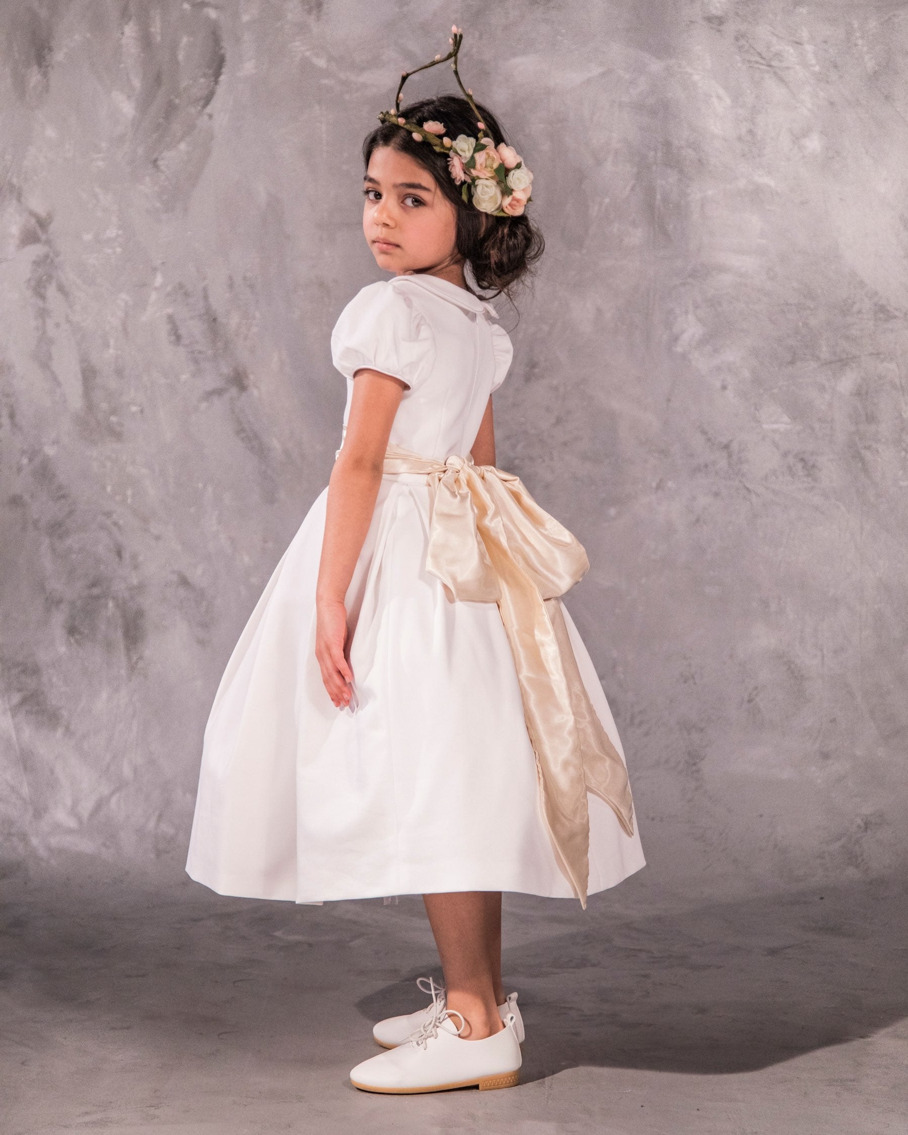 The Rachel – classic flower girl dress with precise seams, puffed sleeves, and a box-pleated skirt. Features a timeless Peter Pan collar, back zip closure, and adjustable petticoat volume. Crafted from satin, silk, and tulle with a silky soft lining, perfect for elegant weddings and special occasions.