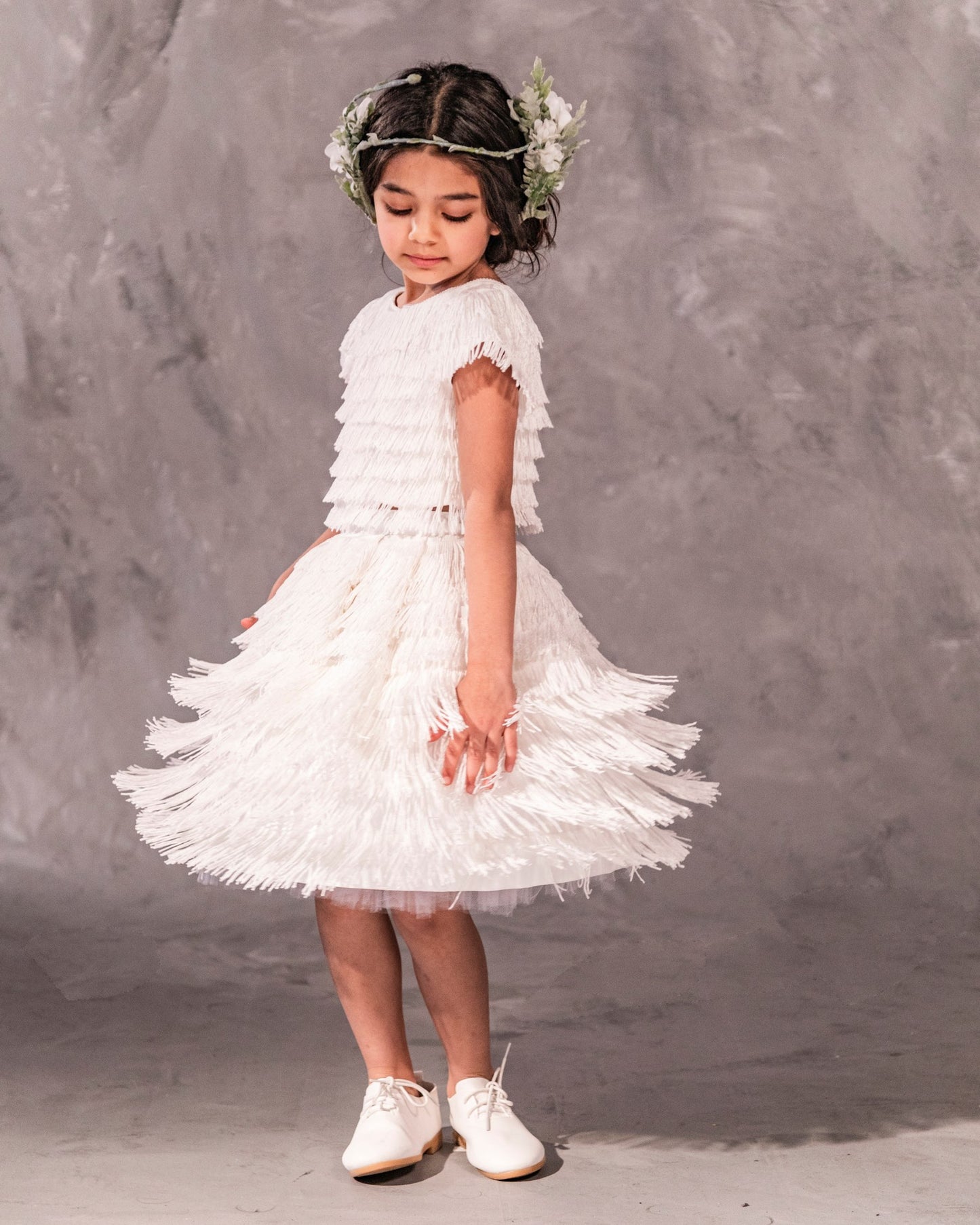 The Vera, a statement two-piece fringe ensemble featuring a cap sleeve top and separate skirt lined with soft tulle. Designed for movement with rows of silky fringe from top to bottom. Fully lined in silk with a back zip closure. Handcrafted in Brooklyn from satin, poly-blend fringe, and silk, with optional personalized embroidery. Perfect for weddings, parties, and special occasions.