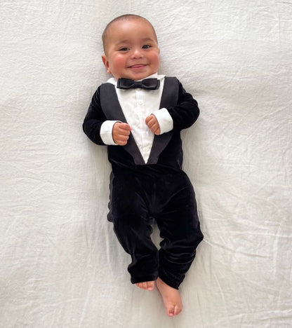 Baby wearing a black tuxedo with a bow tie on a white textured surface
