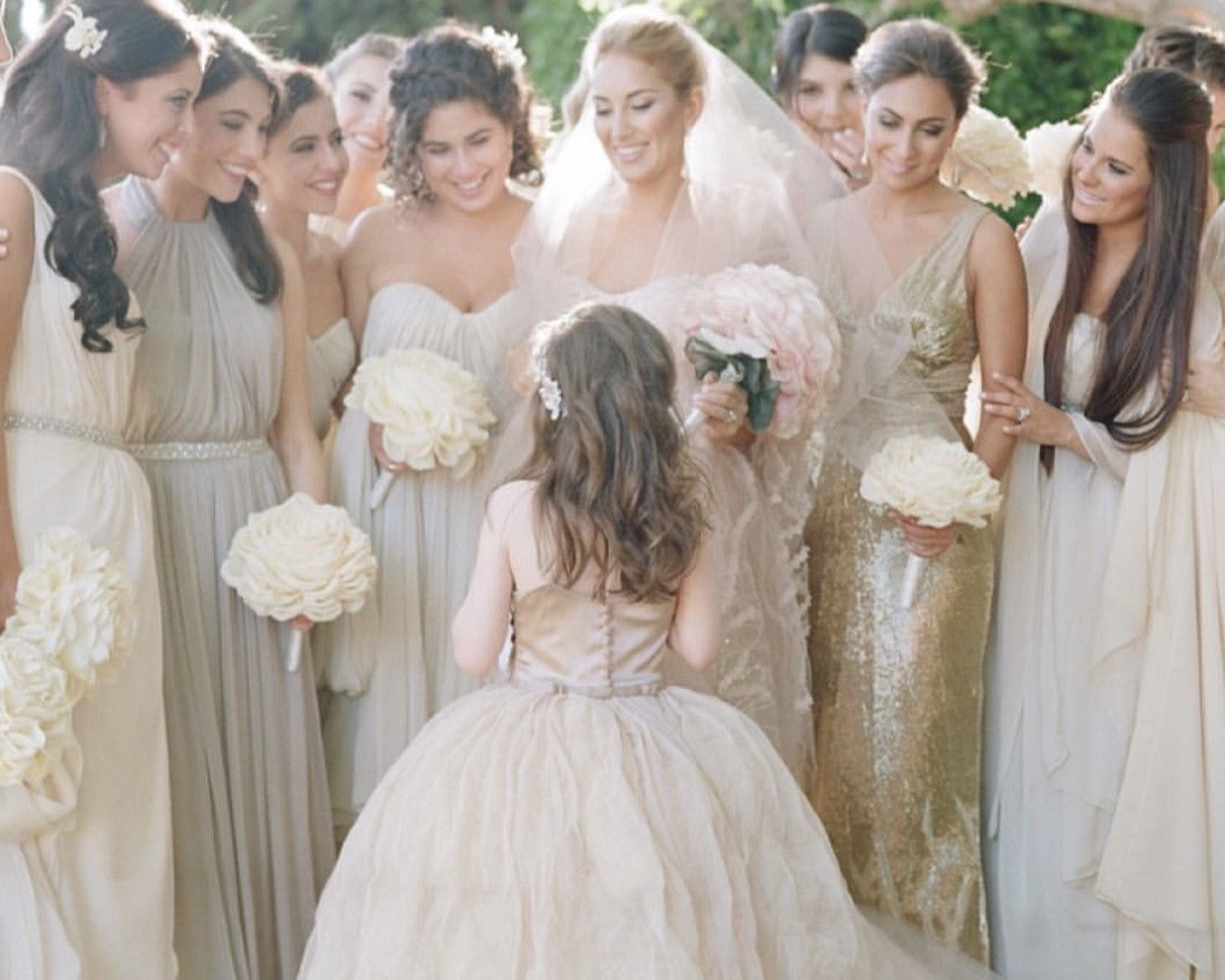 Bride with bridesmaids and a flower girl in formal dresses outdoors.