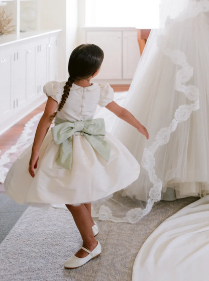 The Rachel VIP satin flower girl dress with pleated skirt, peter pan collar, and covered buttons – elegant choice for weddings and communions. with a beautiful pop up sash