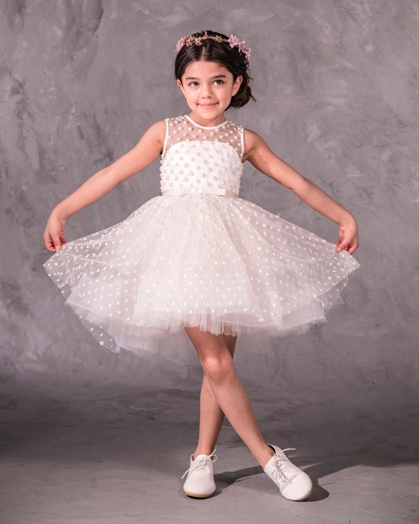 The Pearl flower girl dress featuring intricate pearl embellishments on an illusion neckline and bodice. Swiss dot tulle skirt with a twirly high-low hem, finished with a satin bow. 