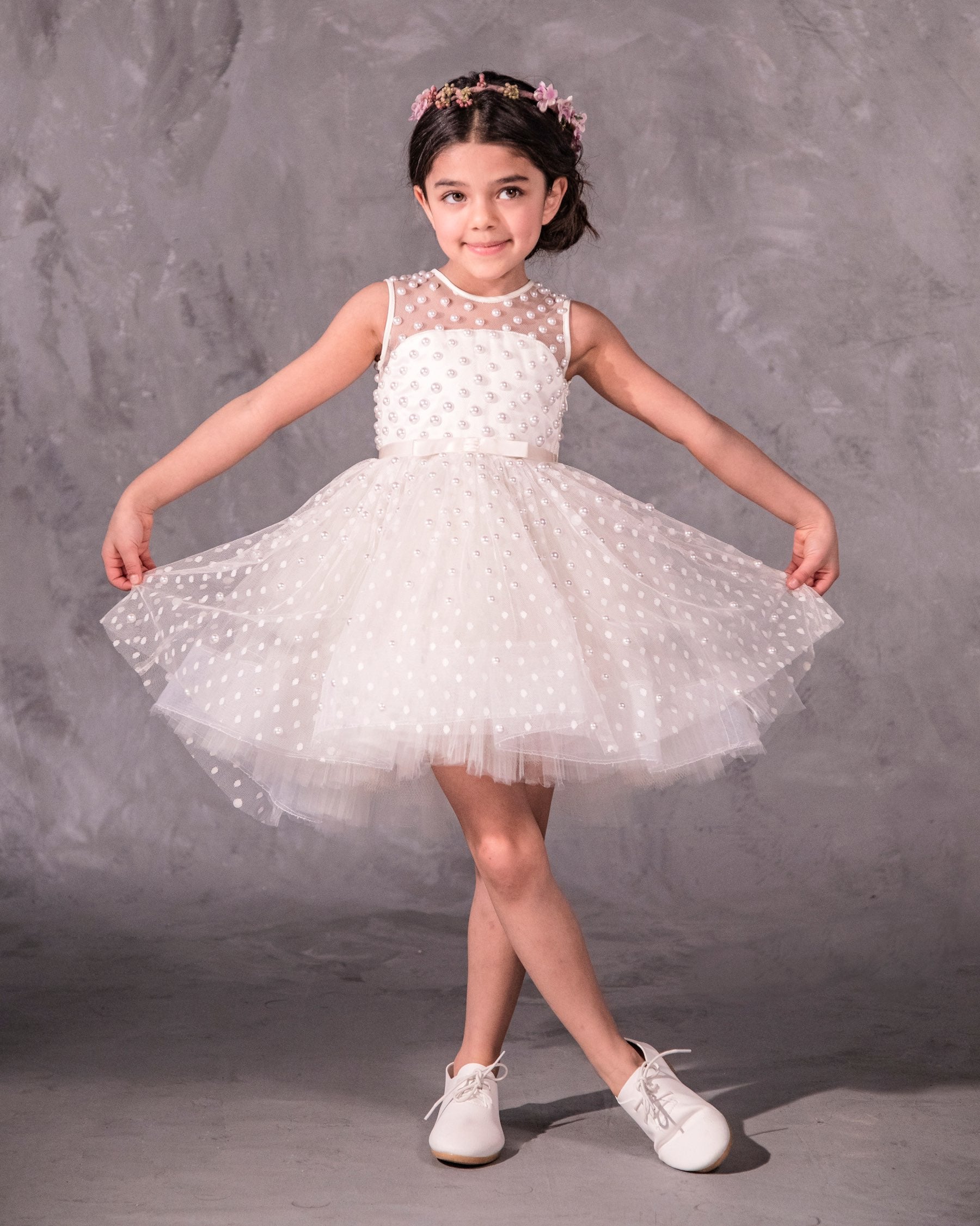 The Pearl flower girl dress featuring intricate pearl embellishments on an illusion neckline and bodice. Swiss dot tulle skirt with a twirly high-low hem, finished with a satin bow. 