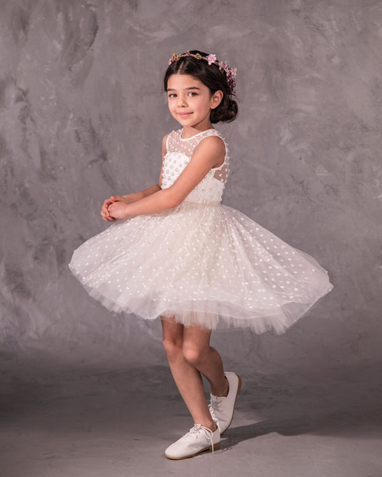 The Pearl flower girl dress featuring intricate pearl embellishments on an illusion neckline and bodice. Swiss dot tulle skirt with a twirly high-low hem, finished with a satin bow. 