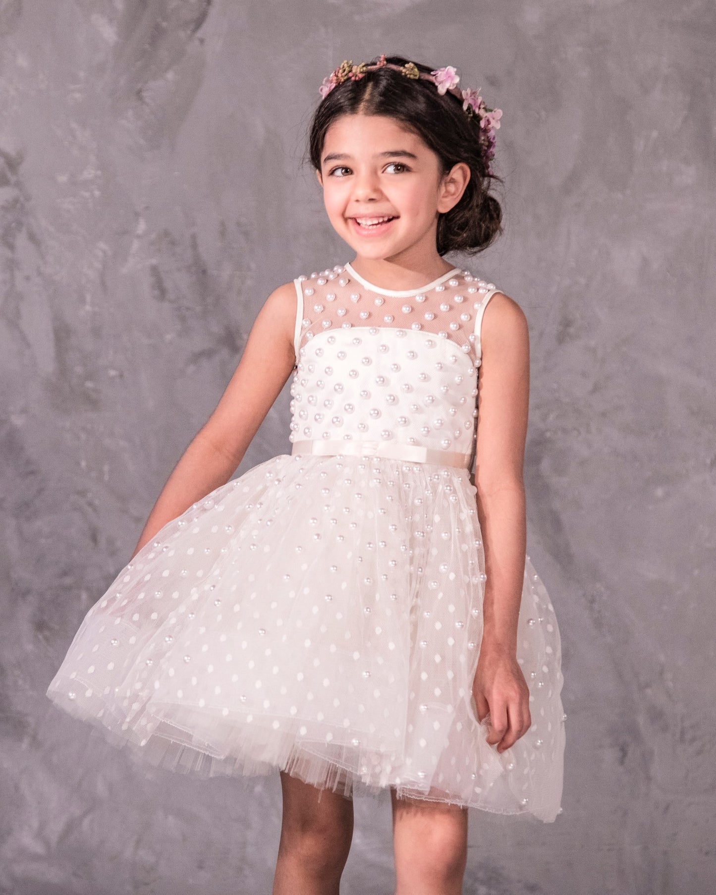The Pearl flower girl dress featuring intricate pearl embellishments on an illusion neckline and bodice. Swiss dot tulle skirt with a twirly high-low hem, finished with a satin bow. 