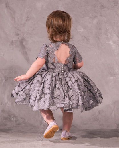 The Baby Annabelle – handcrafted cotton floral lace baby dress with a keyhole back and pearly button closure. Features a full twirl-worthy skirt, silky soft lining, and personalized embroidery. Perfect for first special occasions, weddings, communions, and celebrations
