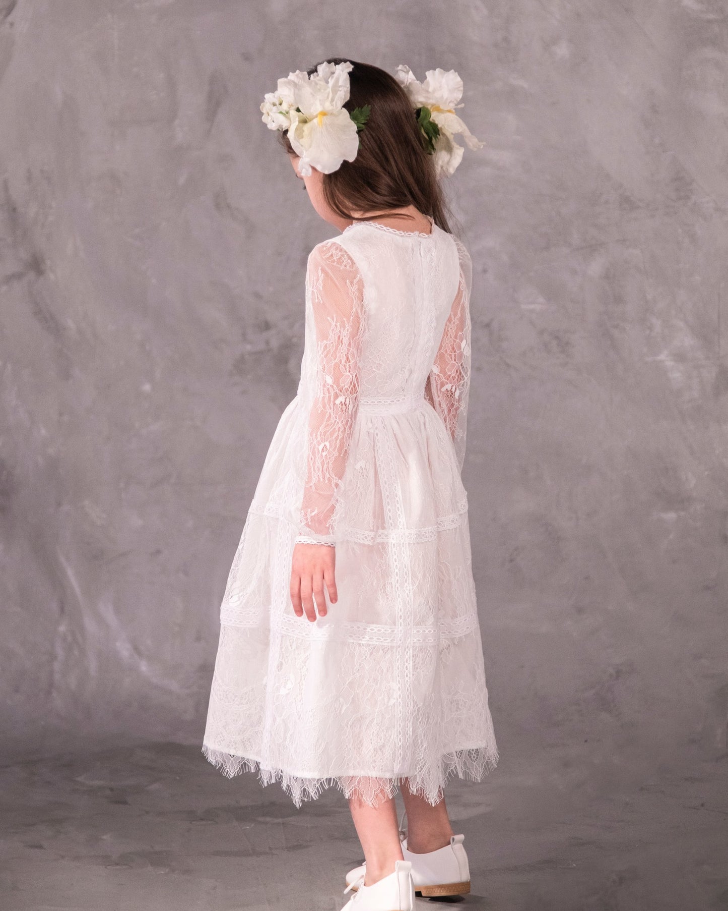 A white, vintage-style dress with sheer sleeves and lace detailing, designed for children, for bohemian and spring-summer weddings