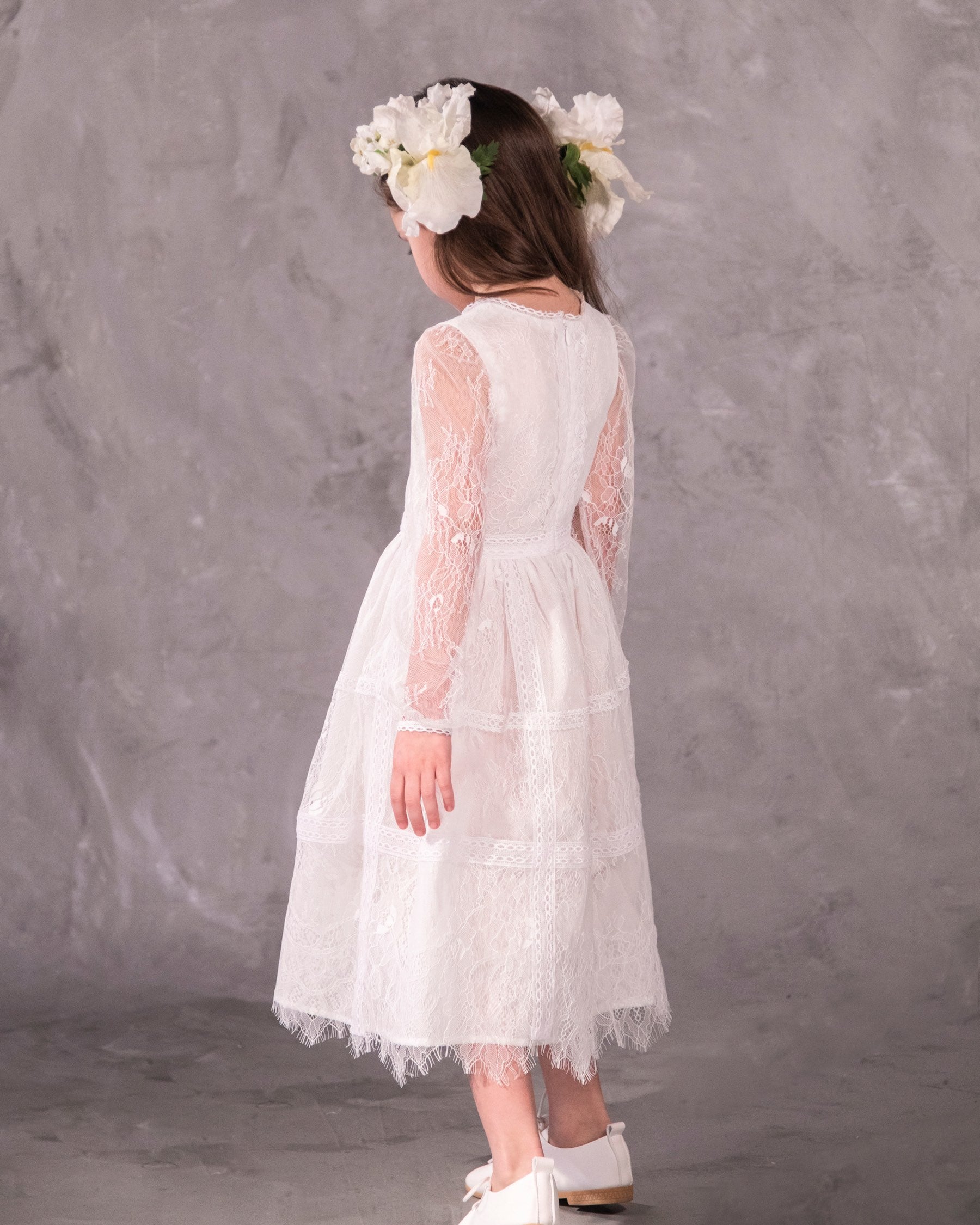 A white, vintage-style dress with sheer sleeves and lace detailing, designed for children, for bohemian and spring-summer weddings