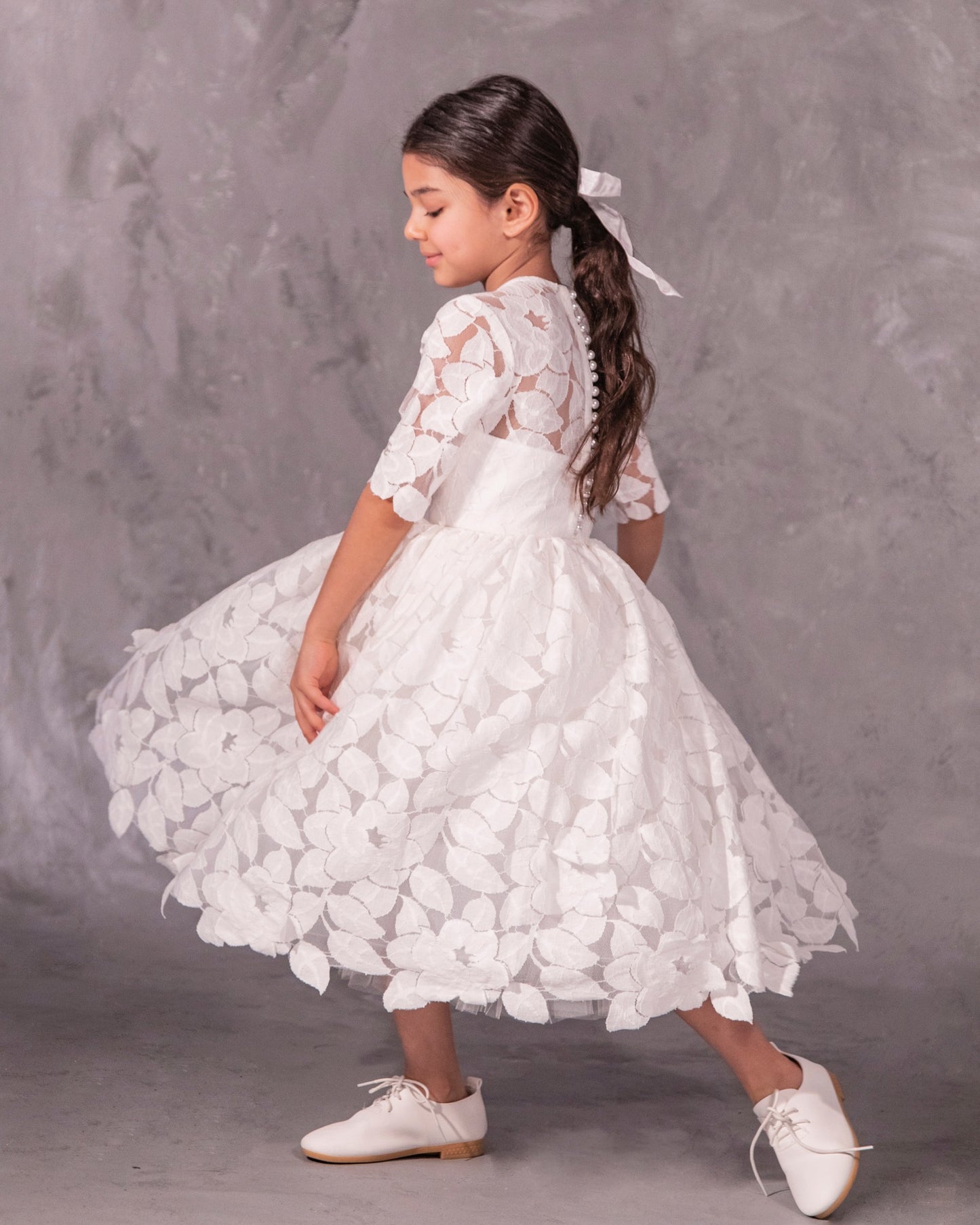 The Isabelle lace flower girl dress with 3/4 long sleeves, tea-length skirt, and pearl button back – ideal for communion and special occasions.