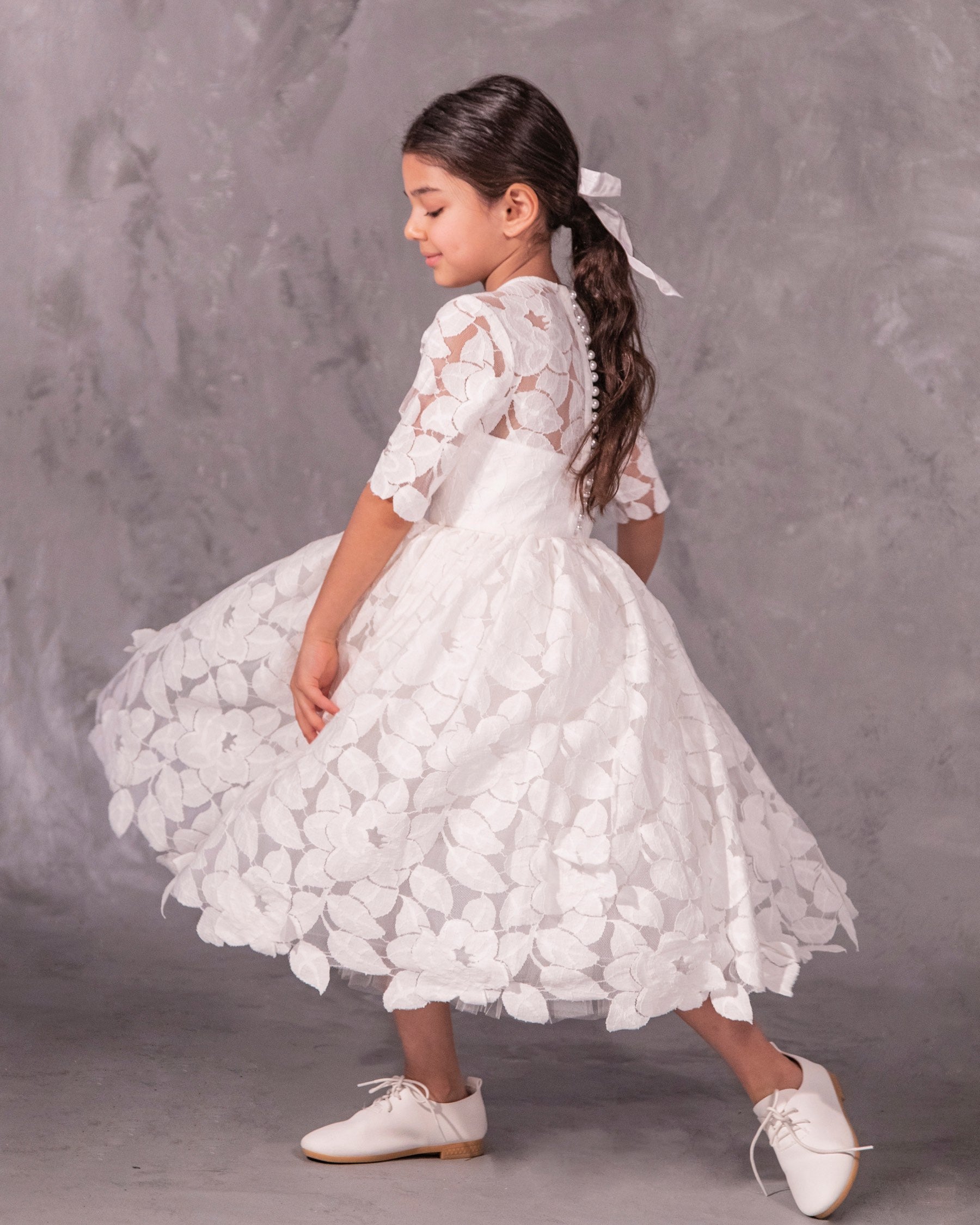 The Isabelle lace flower girl dress with 3/4 long sleeves, tea-length skirt, and pearl button back – ideal for communion and special occasions.