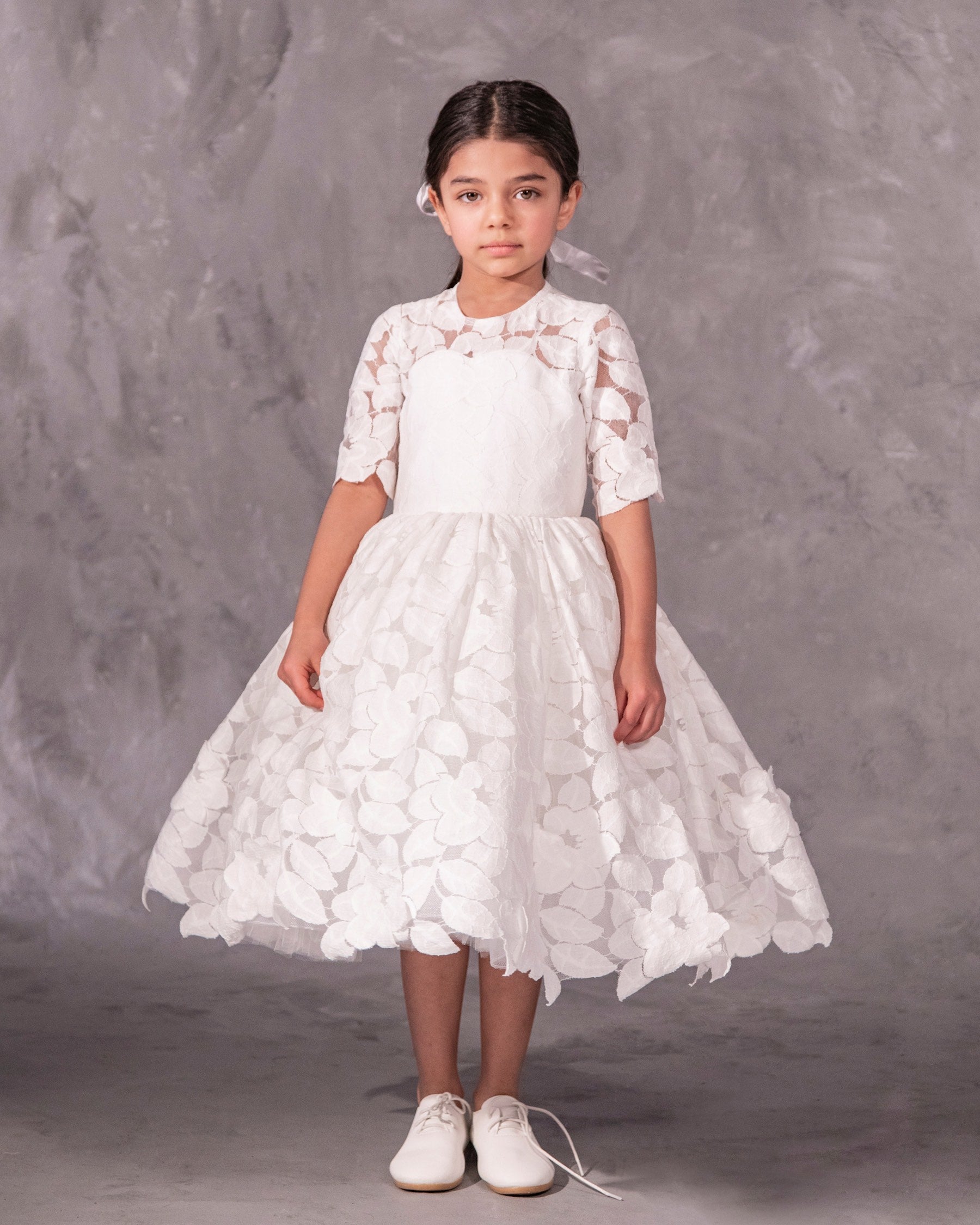The Isabelle lace flower girl dress with 3/4 long sleeves, tea-length skirt, and pearl button back – ideal for communion and special occasions.